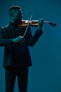 Midsection of man holding violin against clear blue background