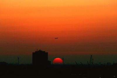 Silhouette birds flying against orange sky