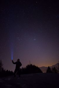 Silhouette man holding illuminated flashlight towards star field sky during night