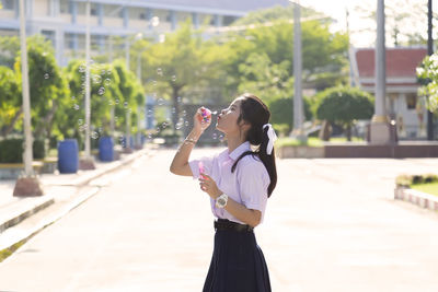 Side view of young woman blowing bubbles on road