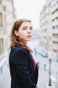 Young woman looking away while standing against city in background