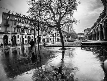 Wet street by canal against buildings in city during rainy season