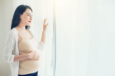 Young woman looking away while standing against wall