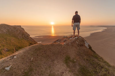 Rear view of man looking at sea against sky during sunset