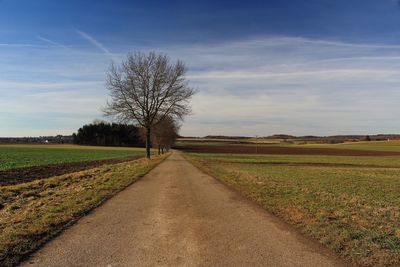 Road amidst field against sky during sunset