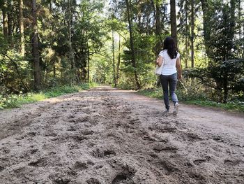 Rear view of woman walking on dirt road in forest