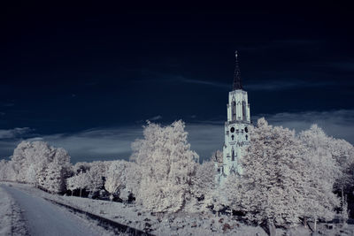 Snow covered road amidst trees and buildings against sky