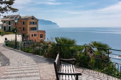 Chairs on footpath by sea against building