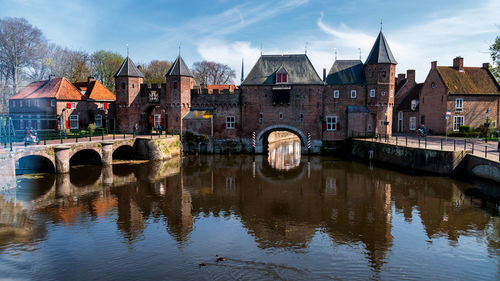 Arch bridge over river by buildings against sky