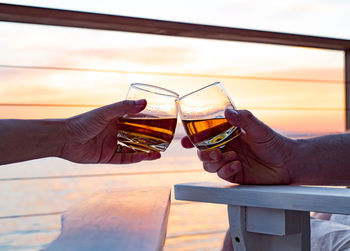 Friends toasting whiskey against sea during sunset