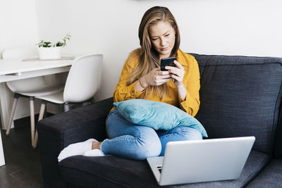 Young woman using mobile phone while sitting on sofa at home