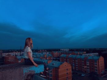 Woman sitting on terrace while looking townscape at dusk