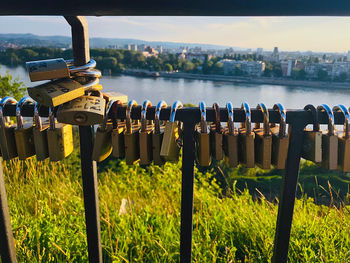 Padlocks on railing by river against sky