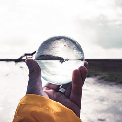 Midsection of person holding crystal ball against sky