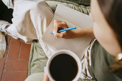 Directly above view of female entrepreneur writing in diary with pen at studio