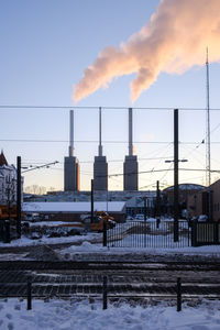 Smoke emitting from snow covered factory against sky