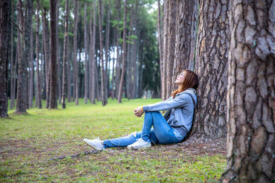 Side view of man sitting on tree trunk in forest