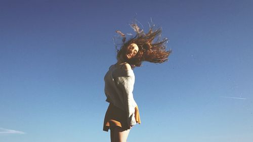 Low angle view of young woman standing against blue sky
