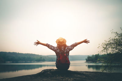 Woman with arms outstretched standing by lake against sky
