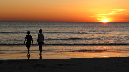 Silhouette children walking at beach against sky during sunset