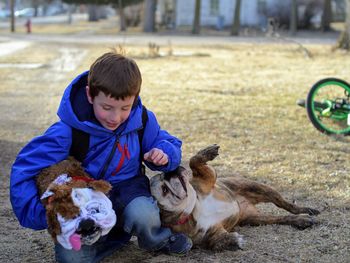 Happy boy holding dog mask playing with english bulldog at park