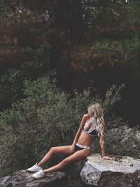 Woman on rock by trees in forest