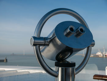Close-up of coin-operated binoculars overlooking sea against blue sky