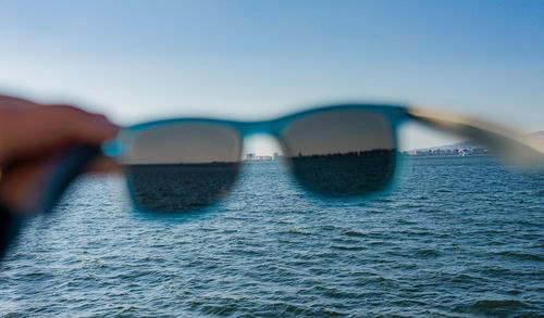 Close-up of sunglasses on sea against clear sky