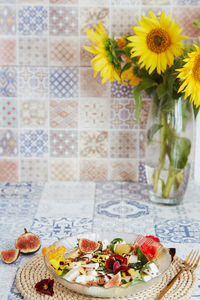 Vegetarian salad with feta, edible flowers, figs, peach, basil on ceramic tile with sunflowers. 