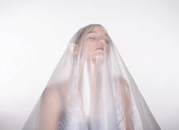 Close-up of woman covered in plastic against white background