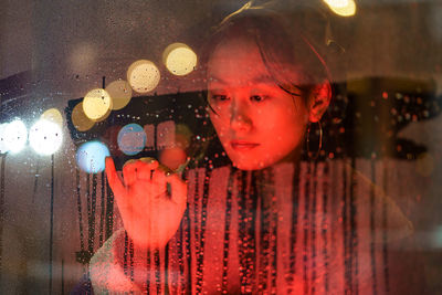 Upset asian girl suffer from solitude alone draw on wet glass in rain after breakup with boyfriend