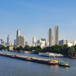 Boats in river by buildings against clear sky