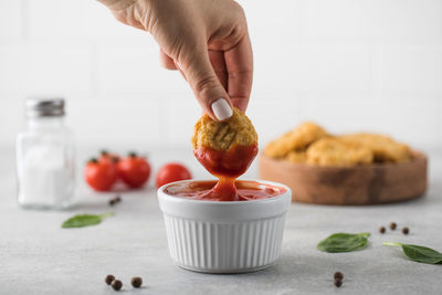 A woman dips a slice of chicken nuggets in ketchup on a light background.