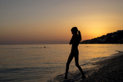 Full length of woman standing on beach against sky during sunset