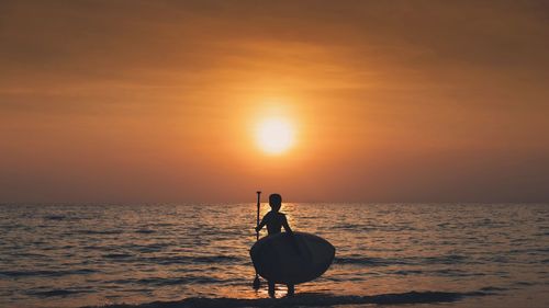 Silhouette people on sea against sky during sunset