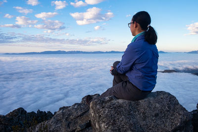 Man sitting on rock looking at sea against sky