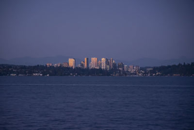 Sea by buildings against clear sky at dusk