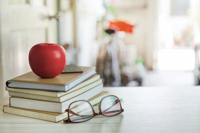 Close-up of books with apple and eyeglasses on table