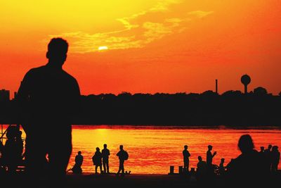 Silhouette people on beach against orange sky