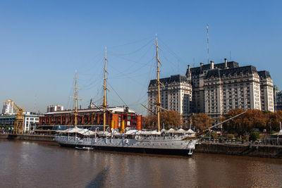 Sailboats in river by buildings against clear sky