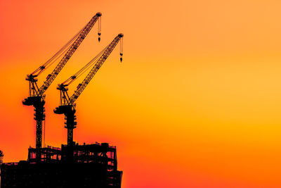 Low angle view of silhouette cranes at construction site against sky during sunset