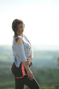 Smiling young woman standing on mountain against clear sky