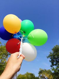 Close-up of hand holding balloons against sky