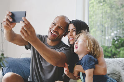 Happy parents taking selfie with son through smart phone on sofa at home