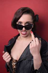 Portrait of young woman showing middle finger against red background