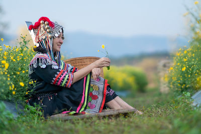 Woman holding umbrella while sitting on field