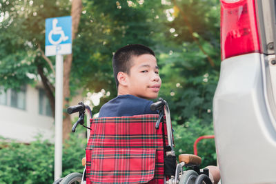 Portrait of boy sitting on wheelchair by car