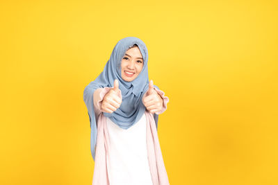 Portrait of smiling young woman against yellow background