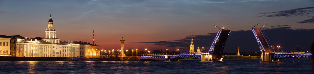 Illuminated buildings by river against sky in city