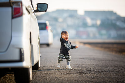 Full length of boy walking on road by car